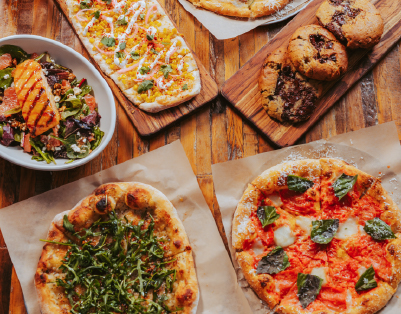 An assortment of dishes from True Food Kitchen's menu, including colorful salads, pizzas, and other fresh items, all beautifully arranged on wooden boards and plates.