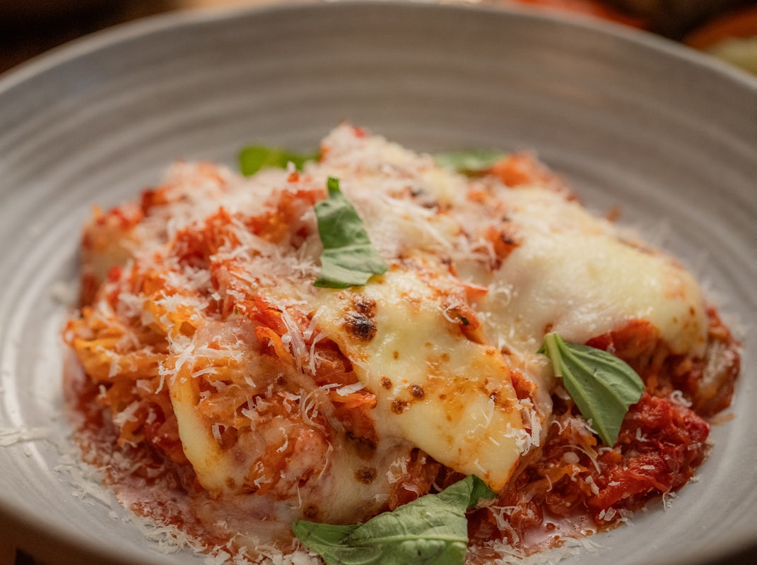 A delicious serving of cheesy lasagna topped with fresh basil, placed in a gray bowl, showcasing a savory blend of tomato sauce and cheese.