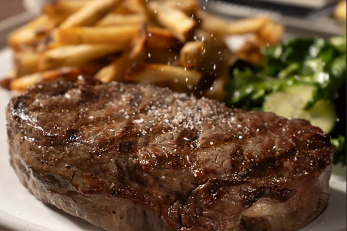 A juicy steak topped with salt is served with crispy fries and fresh green salad on a white plate.