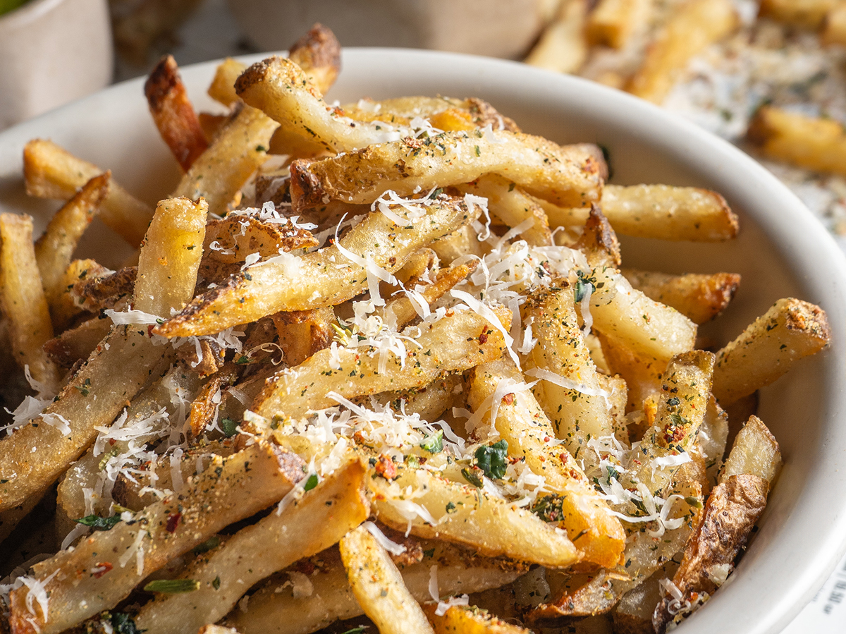 Close-up of a bowl filled with seasoned French fries topped with grated cheese and herbs, creating a savory and appetizing dish.