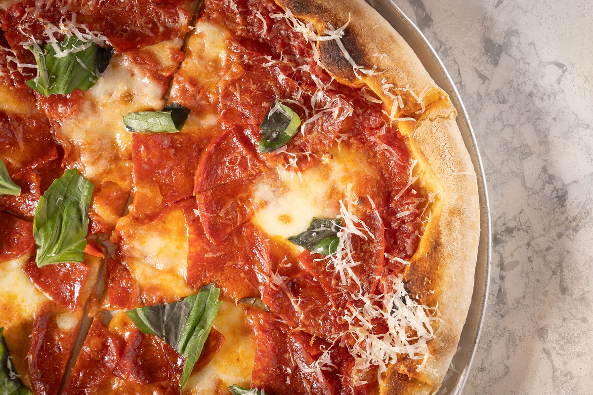 Close-up view of a delicious pizza with pepperoni, fresh basil, melted cheese, and crispy crust on a marble table surface.